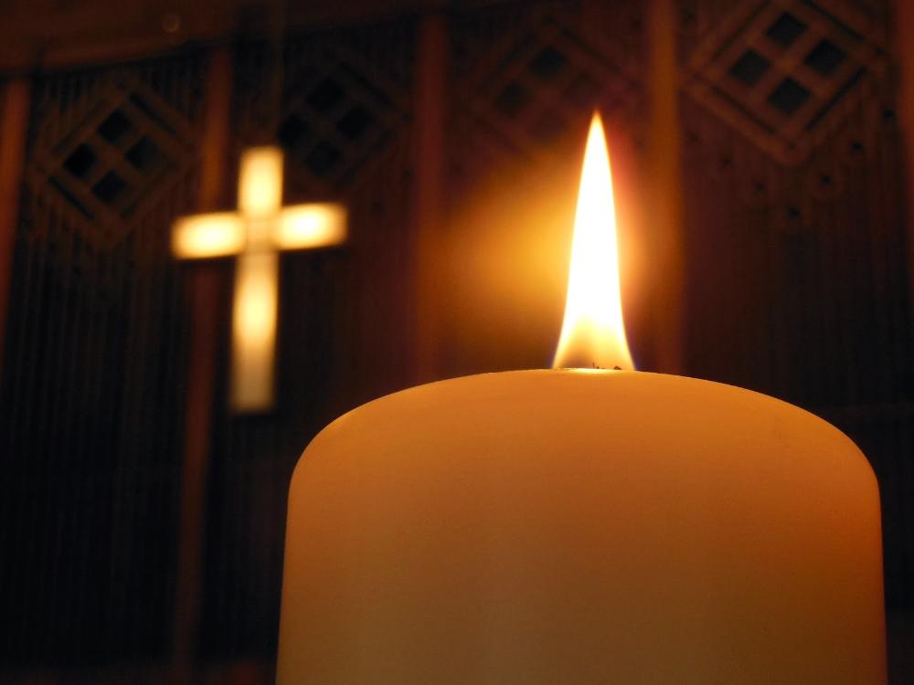 Palava kynttilä ja seinillä valaistu risti