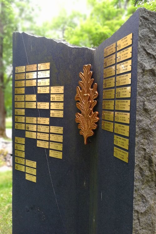 Sotaveteraanien muistokivi, jossa nimilaattoja. Taustalla lehtipuita.
