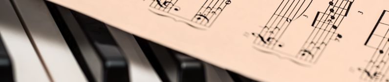 Lähikuva pianon koskettimista, joiden päällä osittain jonkin kappaleen nuotit.