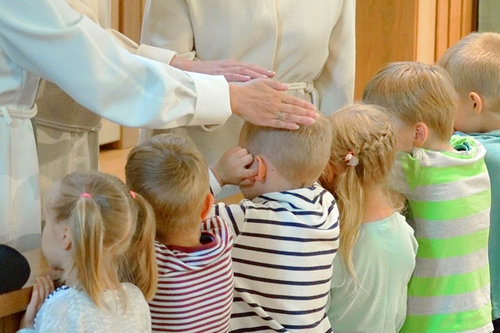 Lapsia alttarilla siunattavana. Papit siunaavat yhtä lapsista panemalla kädet hänen päänsä päälle.